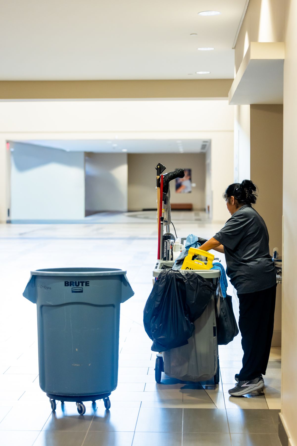 A professional cleaner working with a fully stocked cleaning cart in a bright commercial building