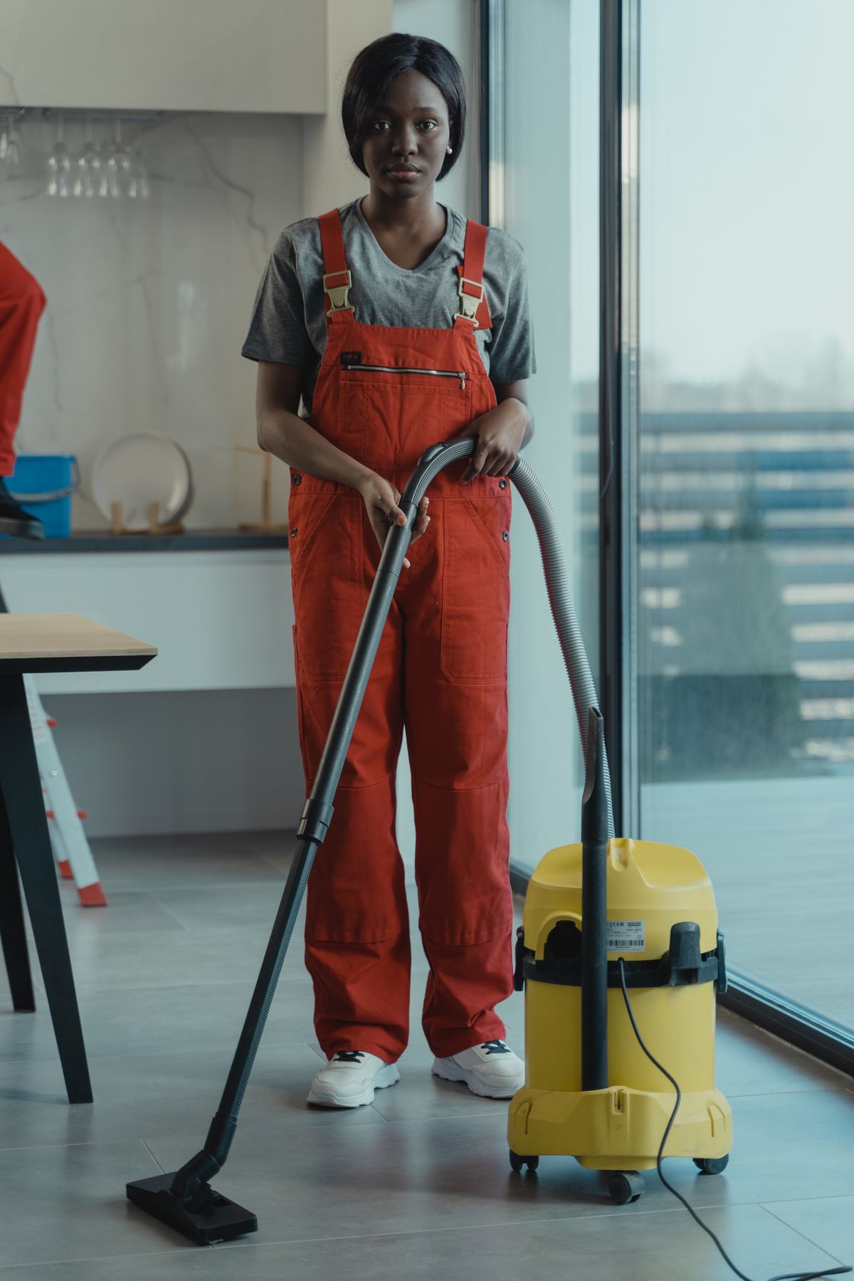 A professional cleaner in uniform vacuuming the floor of a modern office
